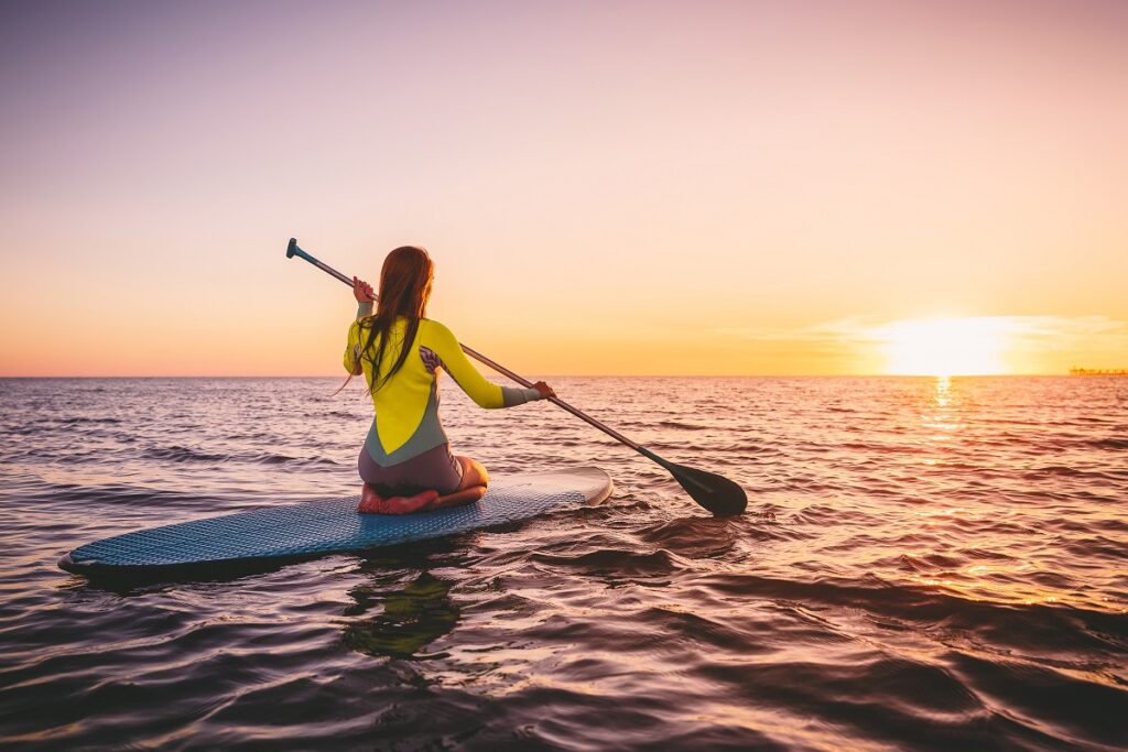Girl on stand up paddle board, quiet sea with warm sunset colors. Relaxing on ocean content-image